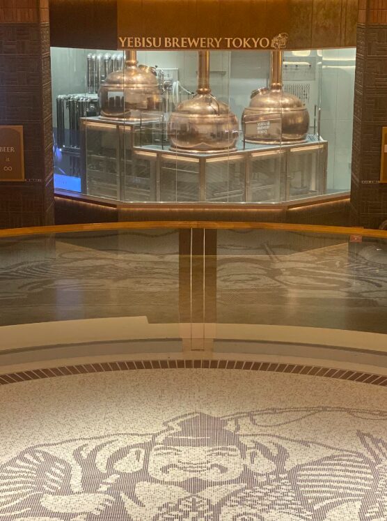 YEBISU BREWERY TOKYOのガラス越しに見える醸造設備と床面のヱビス意匠