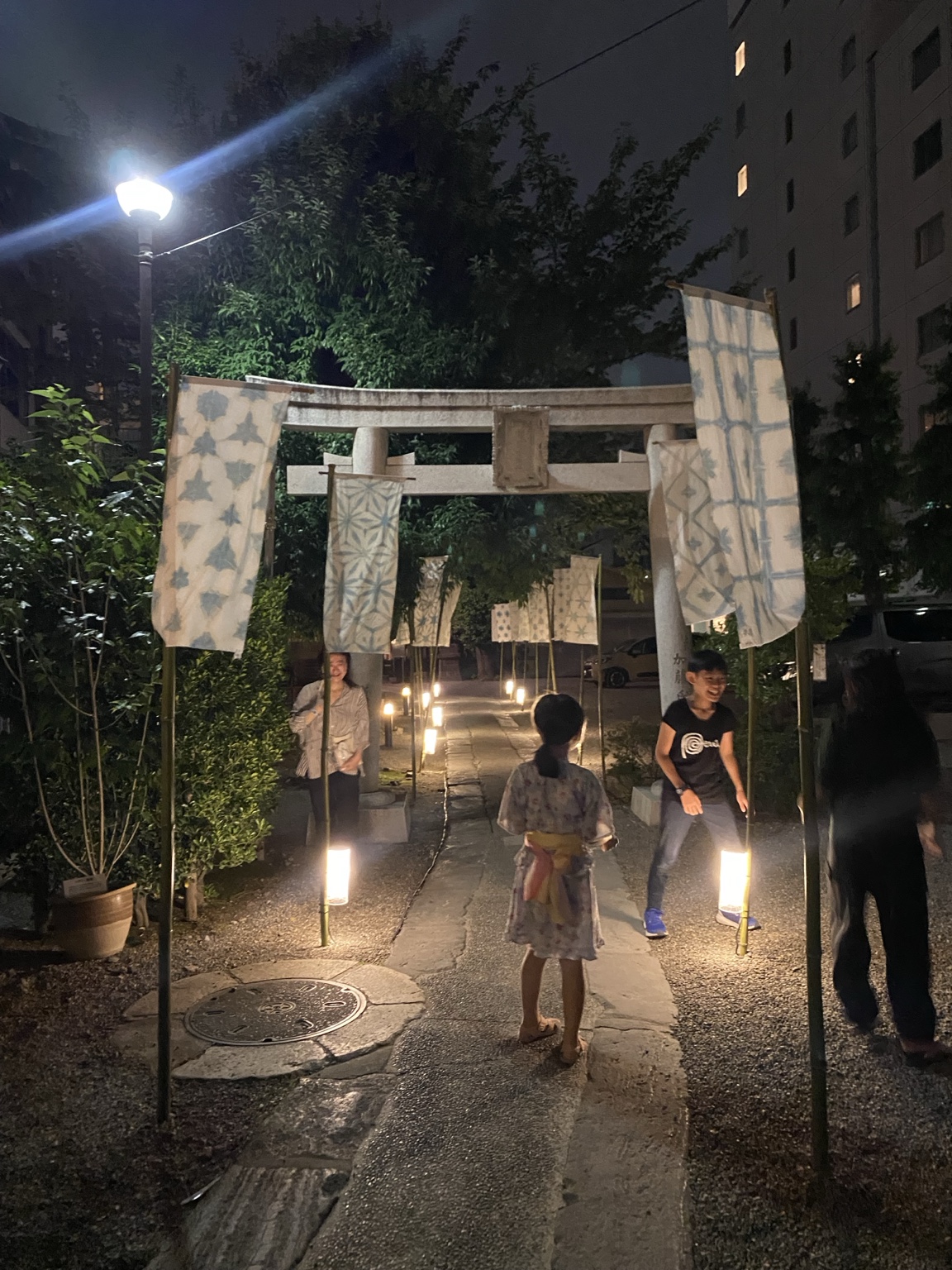 夜の被官稲荷神社参道に立つ鳥居と染め布、灯り