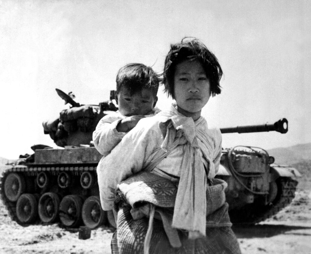 1951年、弟を背負って戦車の横を歩く朝鮮人避難民の少女