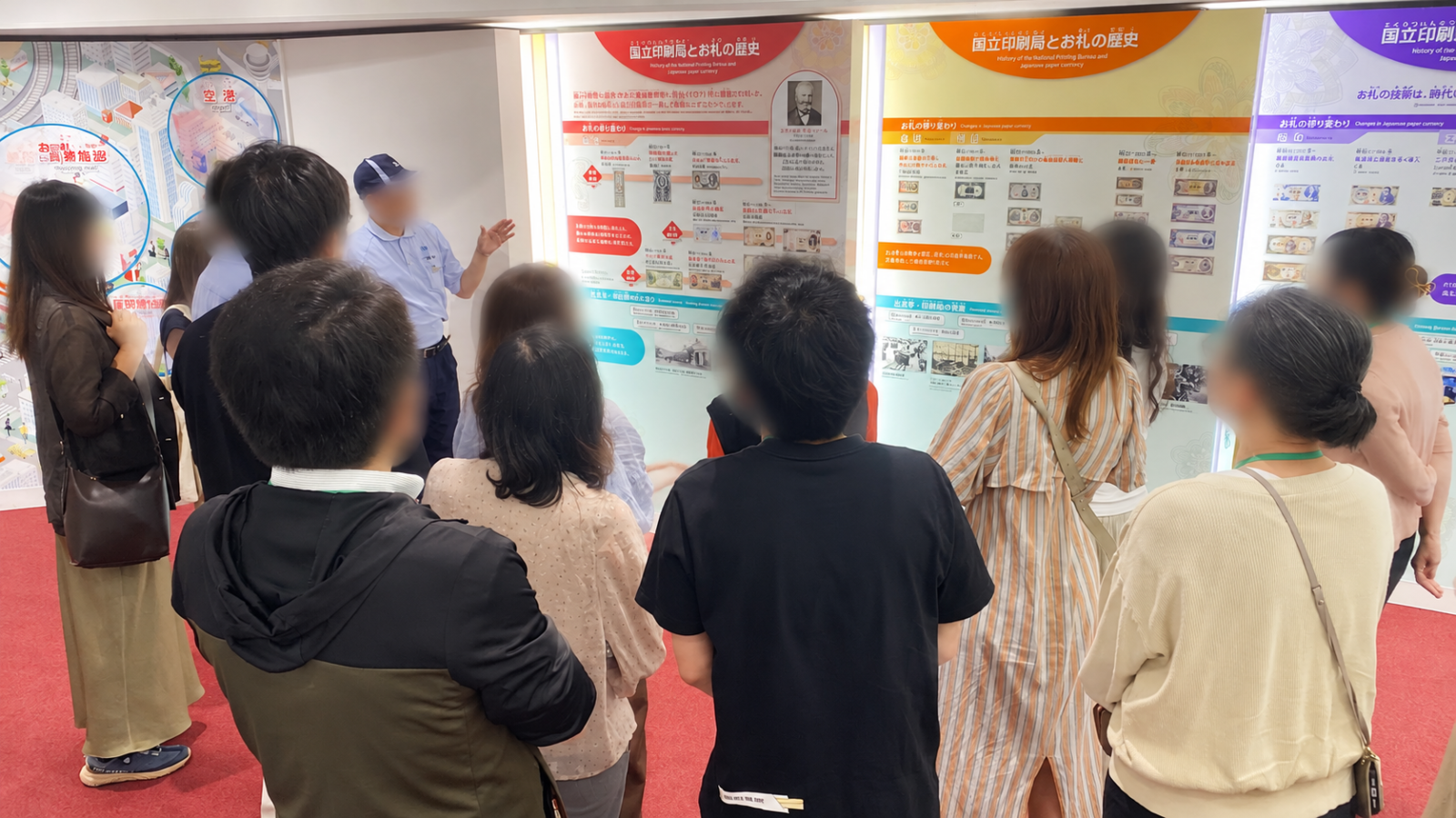 国立印刷局東京工場の展示室で紙幣の歴史説明を聞く見学者