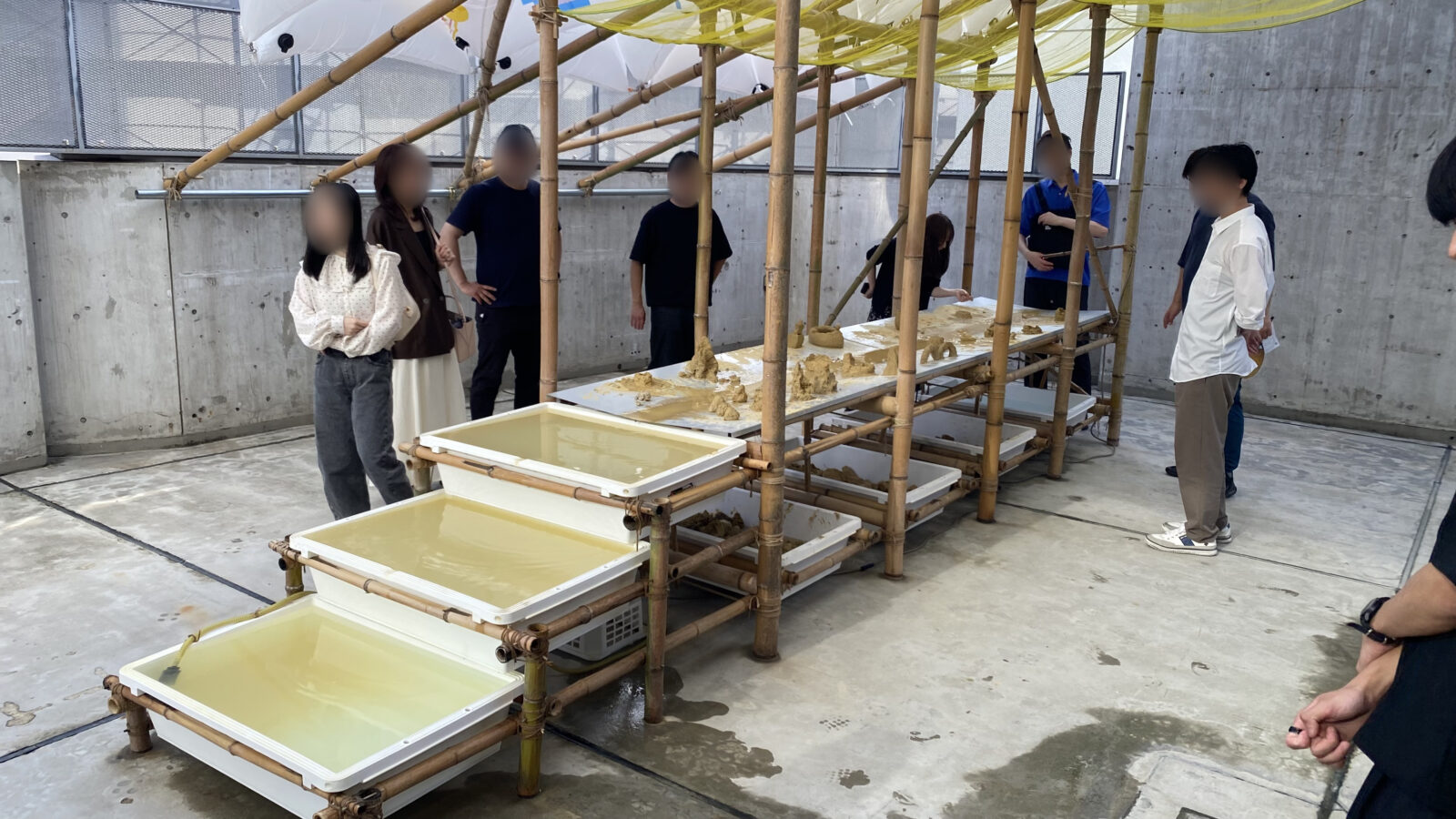 竹組みと泥と水の展示を囲んで鑑賞する参加者たち