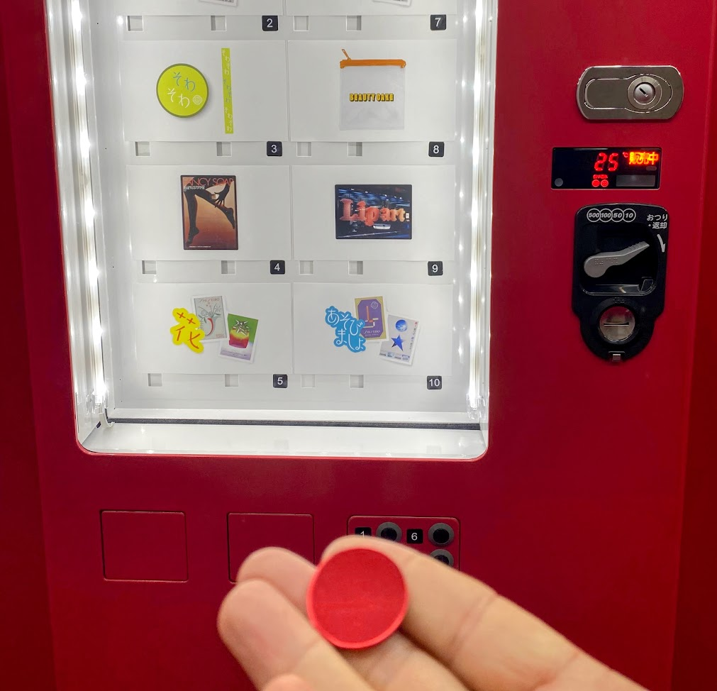 「ディグる?」3階のノベルティ自販機で赤いカプセルを受け取った様子
