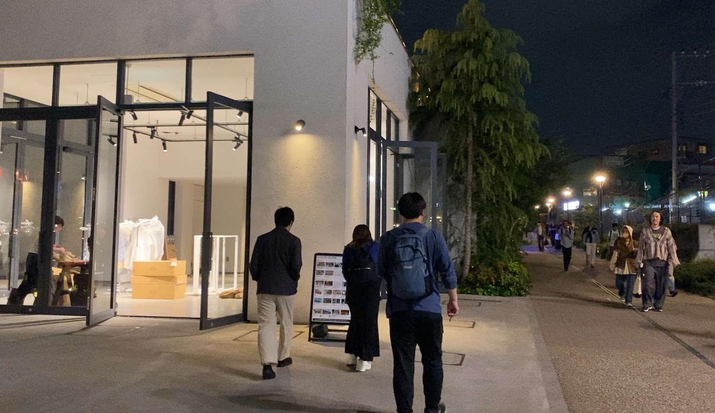 夜の下北線路街reload、白い建物のガラス張りの店舗入口と歩行者が行き交う通路