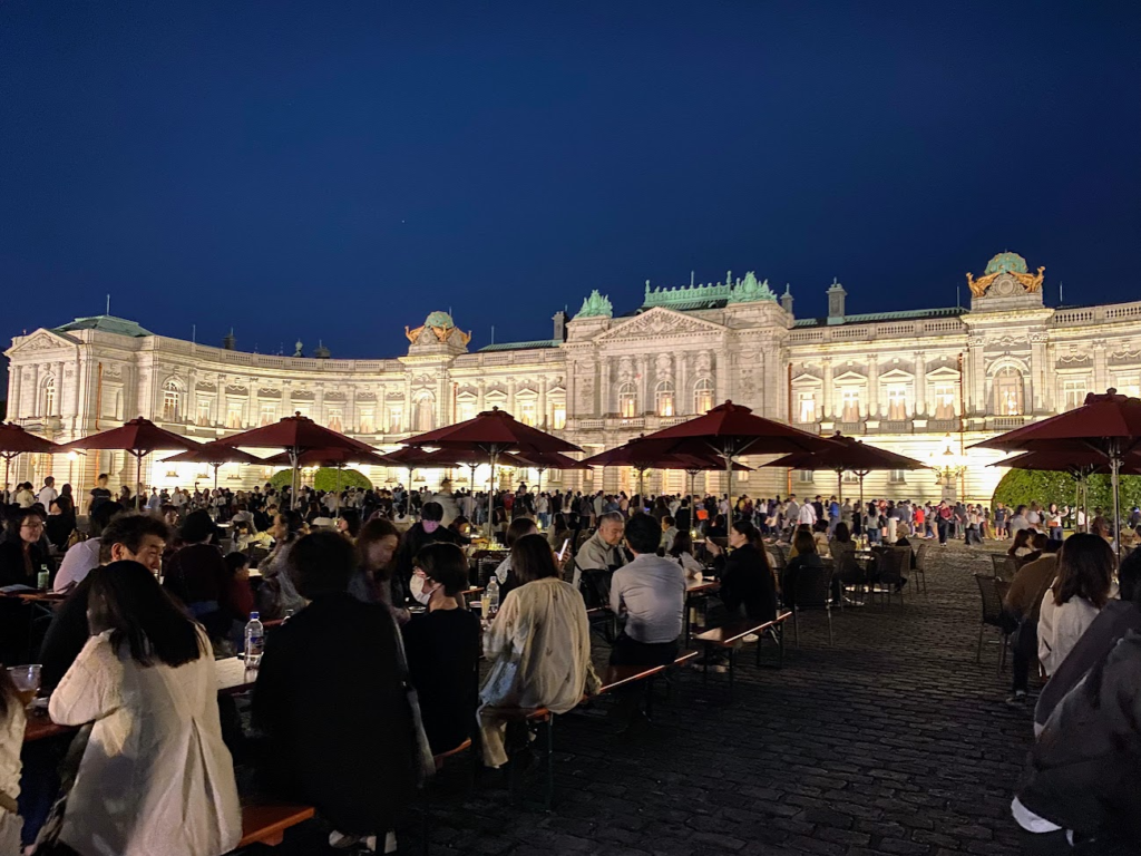 迎賓館赤坂離宮前庭のガーデンカフェで飲食を楽しむ来場者とライトアップ本館