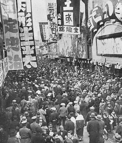 1934年の浅草六区。劇場の看板が立ち並ぶ街路を大勢の人が歩いている