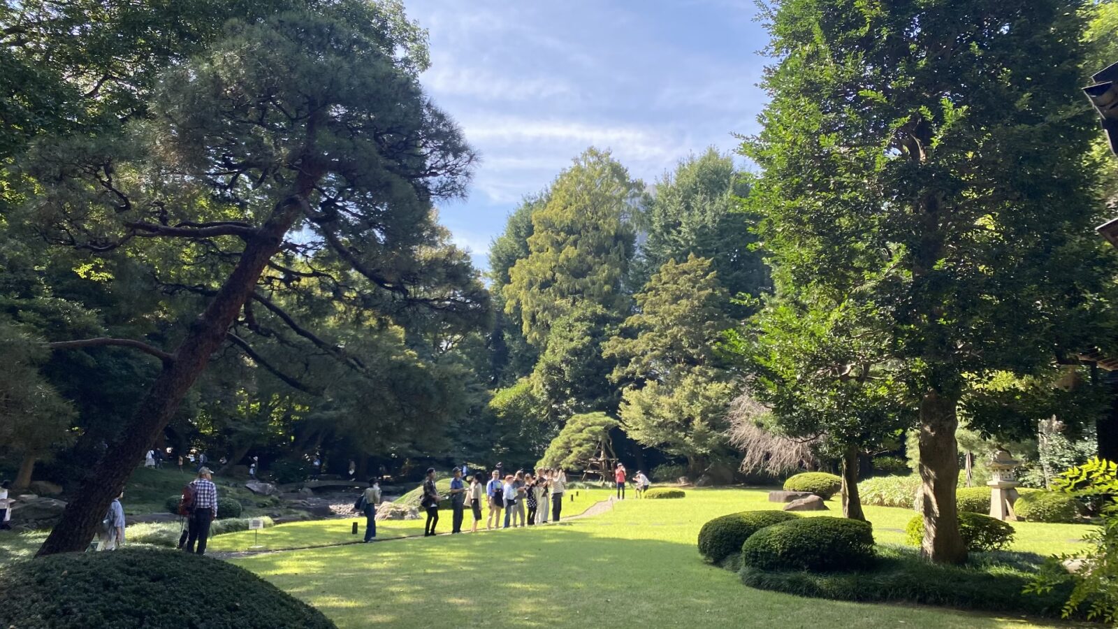 懐徳館庭園に入った直後の明るい芝庭と樹木、散策する人々